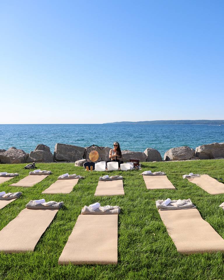 Tan mats laid out on grass for lakefront sound bathing class, with quartz bowls, gong, instructor