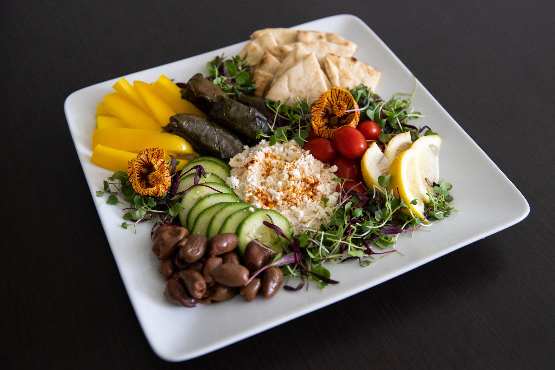 Mediterranean Platter with fresh veggies, hummus, and pita, with lemon slices on square plate