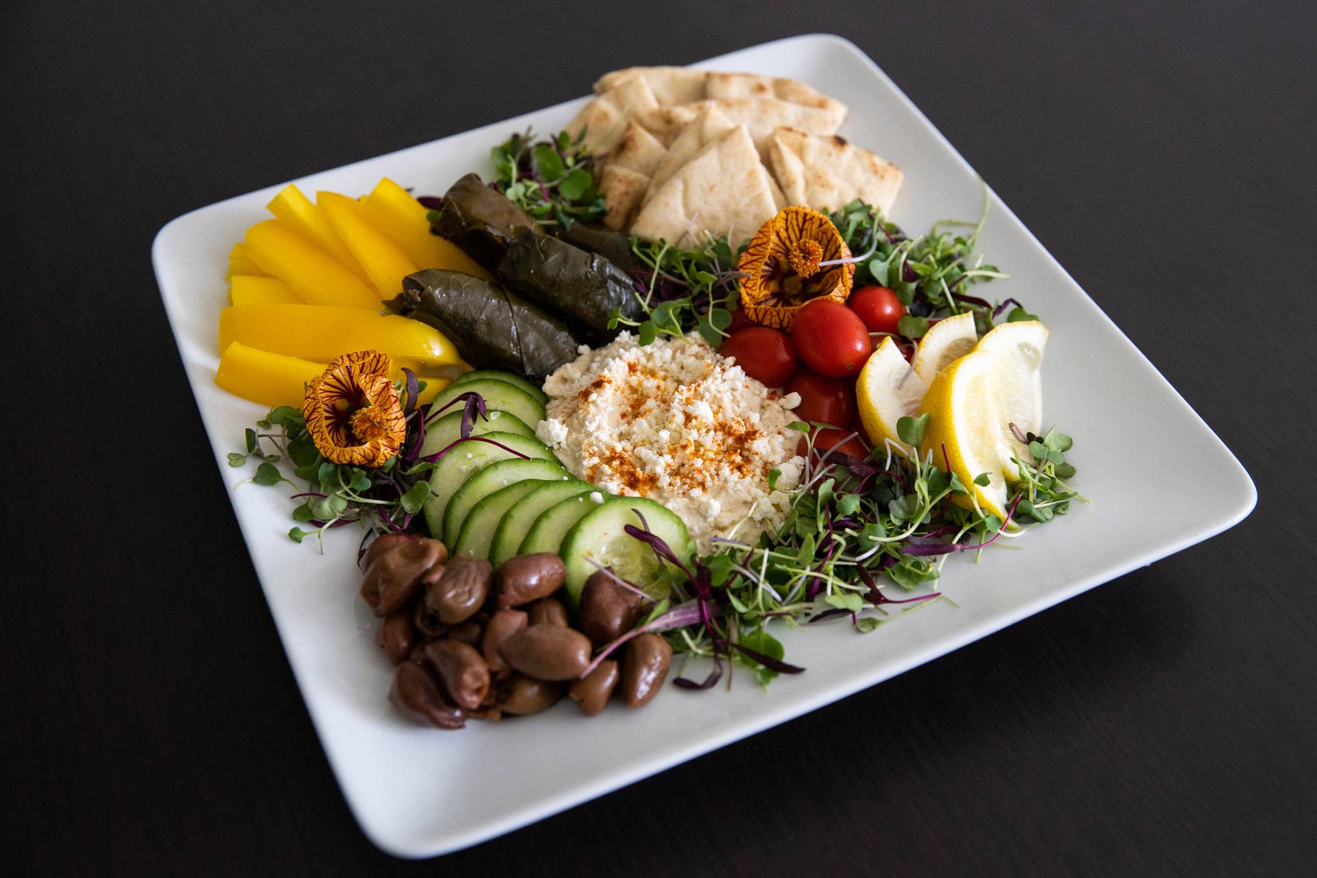 Mediterranean Platter with fresh veggies, hummus, and pita, with lemon slices on square plate