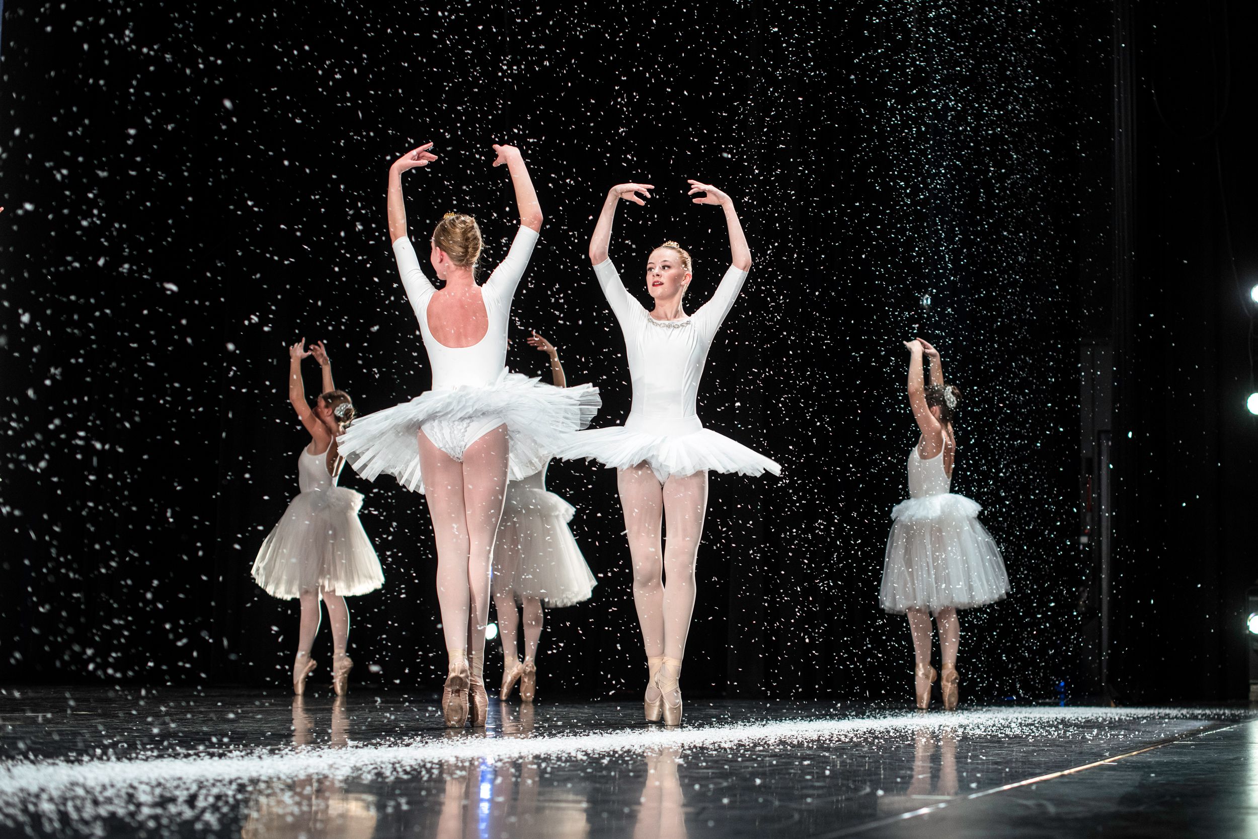 Ballet students in white tutus perform on stage under falling snow, The Nutcracker