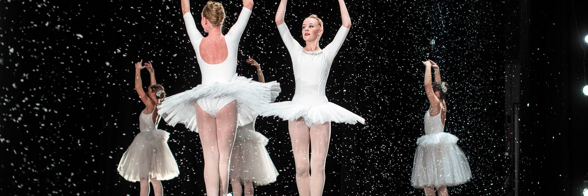 Ballet students in white tutus perform on stage under falling snow, The Nutcracker
