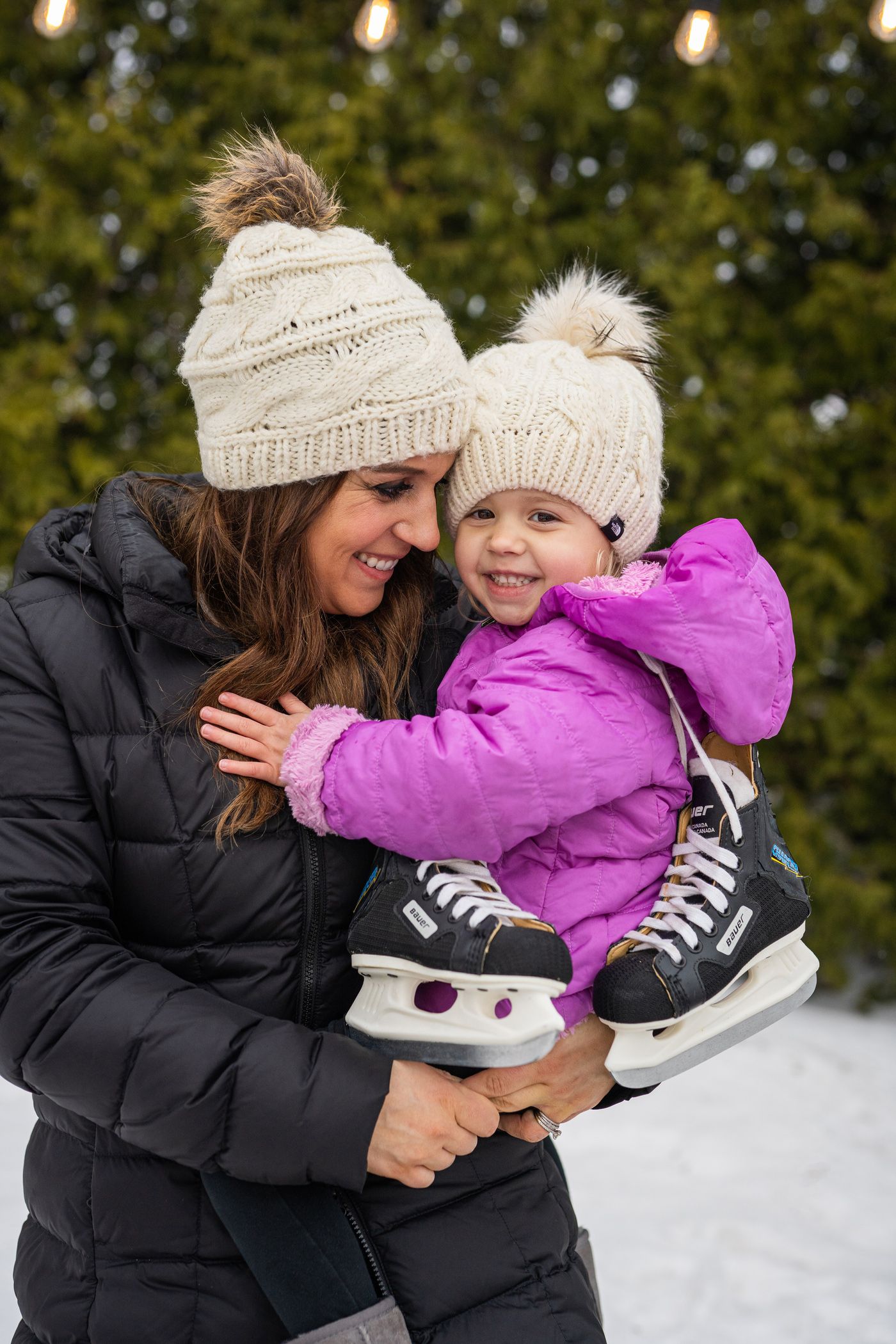 Young mother daughter wearing winter hats snuggle smile holding ice skates