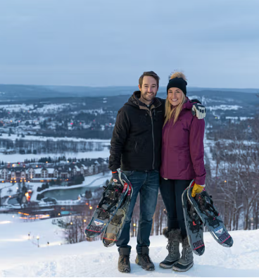 Couple holding snowshoes smiles for photo at top of Boyne Mountain