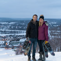 Couple holding snowshoes smiles for photo at top of Boyne Mountain