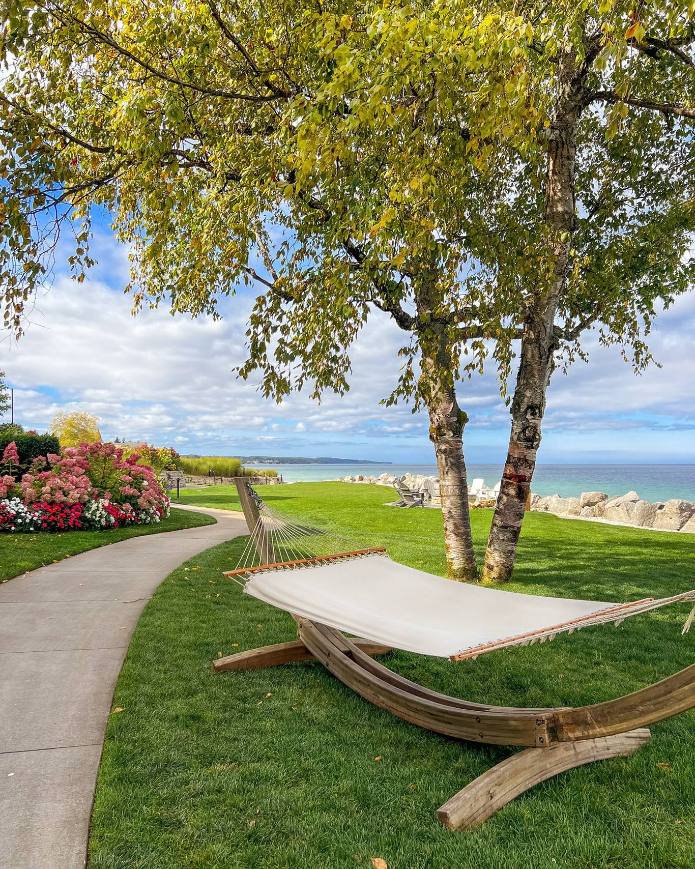 White, wood hammock on green grass under fall birch tree near gardens and rocky shore of Lake Michigan