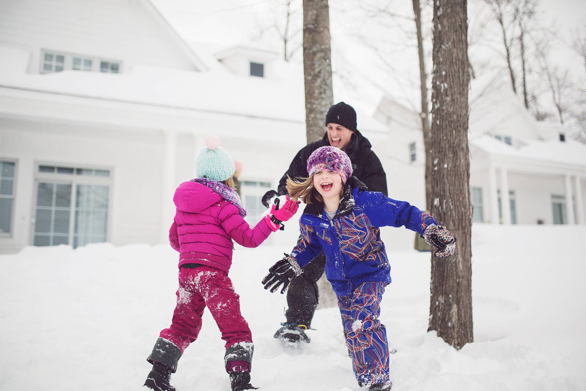 Family laughs and plays in snow by Crooked Tree Cottages