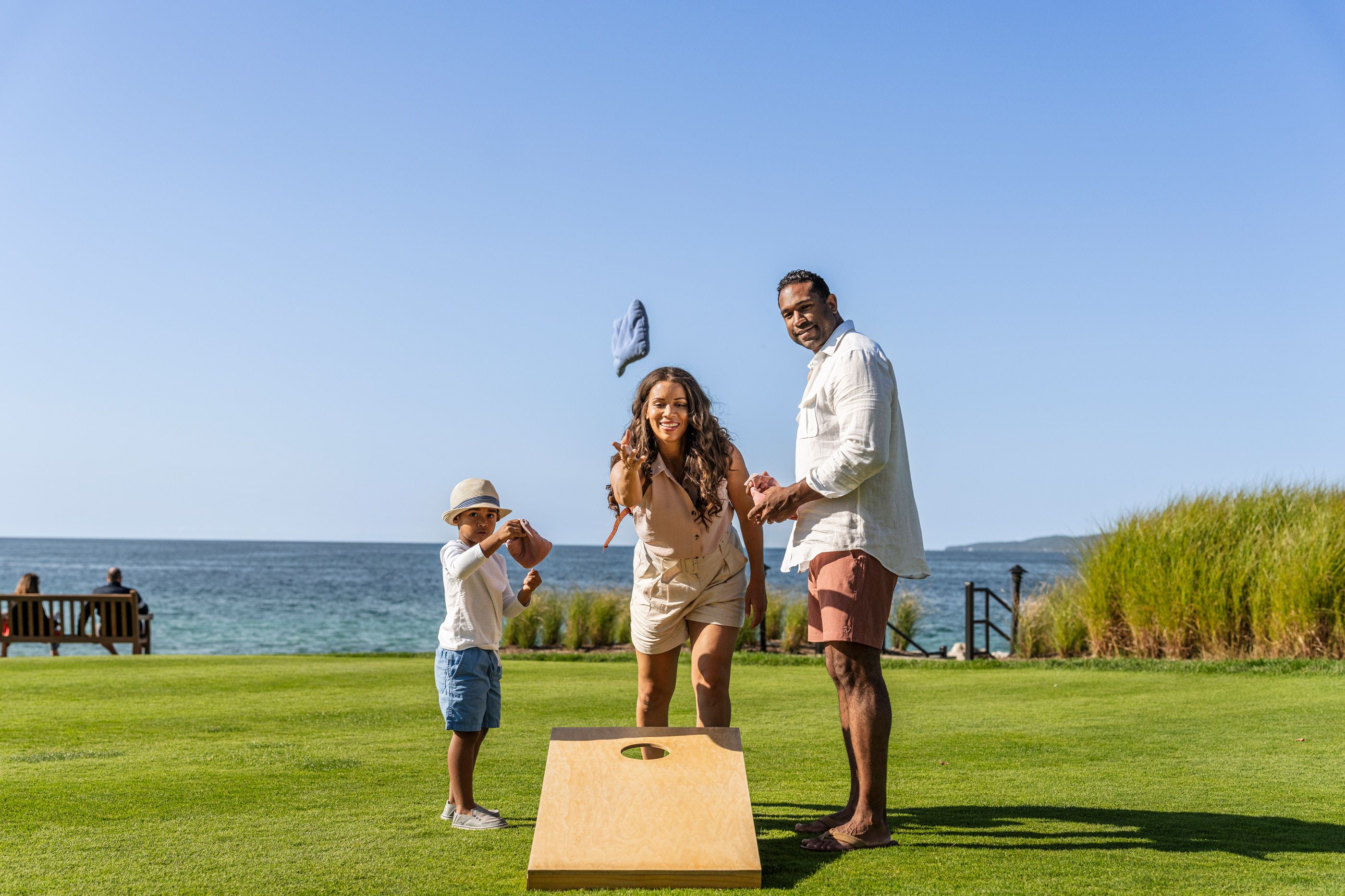 Parents and young son smile as mom tosses bean bag for cornhole lawn game near Lake Michigan, Inn at Bay Harbor