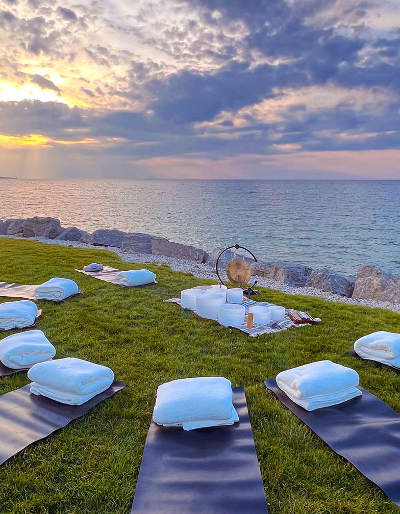 Mats and quartz singing bowls setup for sound healing on grass along Lake Michigan at sunset