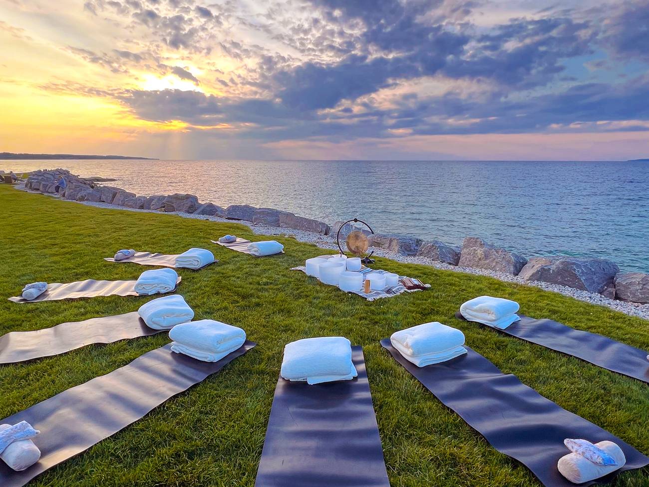 Mats and quartz singing bowls setup for sound healing on grass along Lake Michigan at sunset