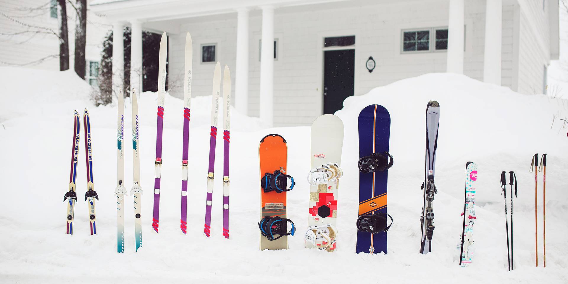 Skis and snowboards line up in front of a Cottage in the wintertime