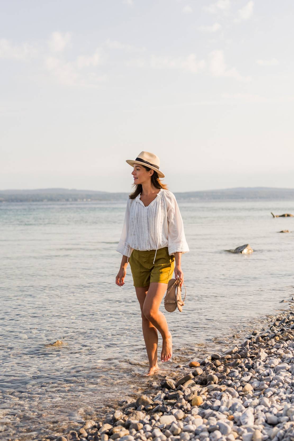 Young woman strolling along the rocky shoreline of Lake Michigan near Inn at Bay Harbor during daytime.