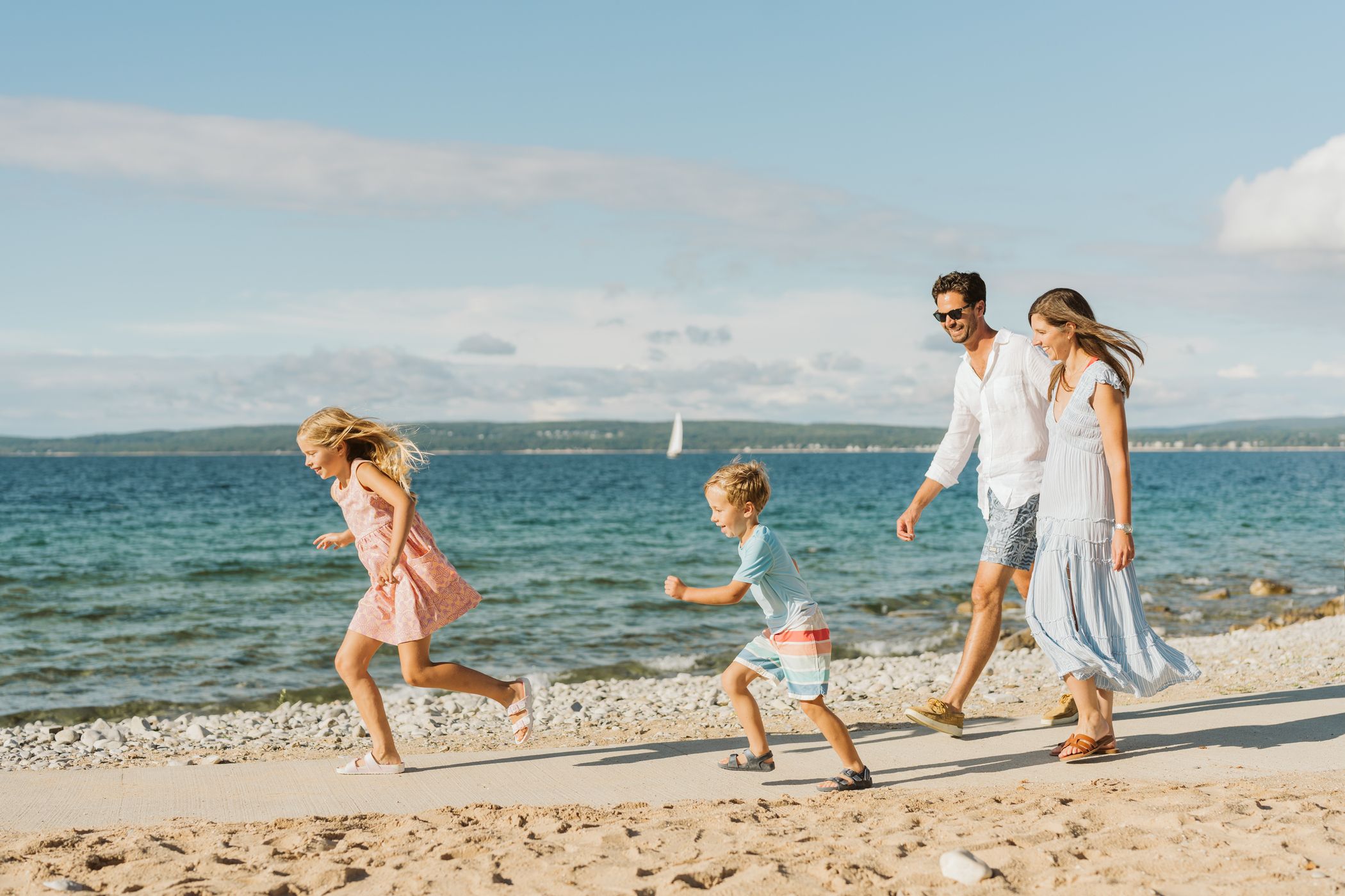 Smiling parents look on as kids run along waterfront sidewalk