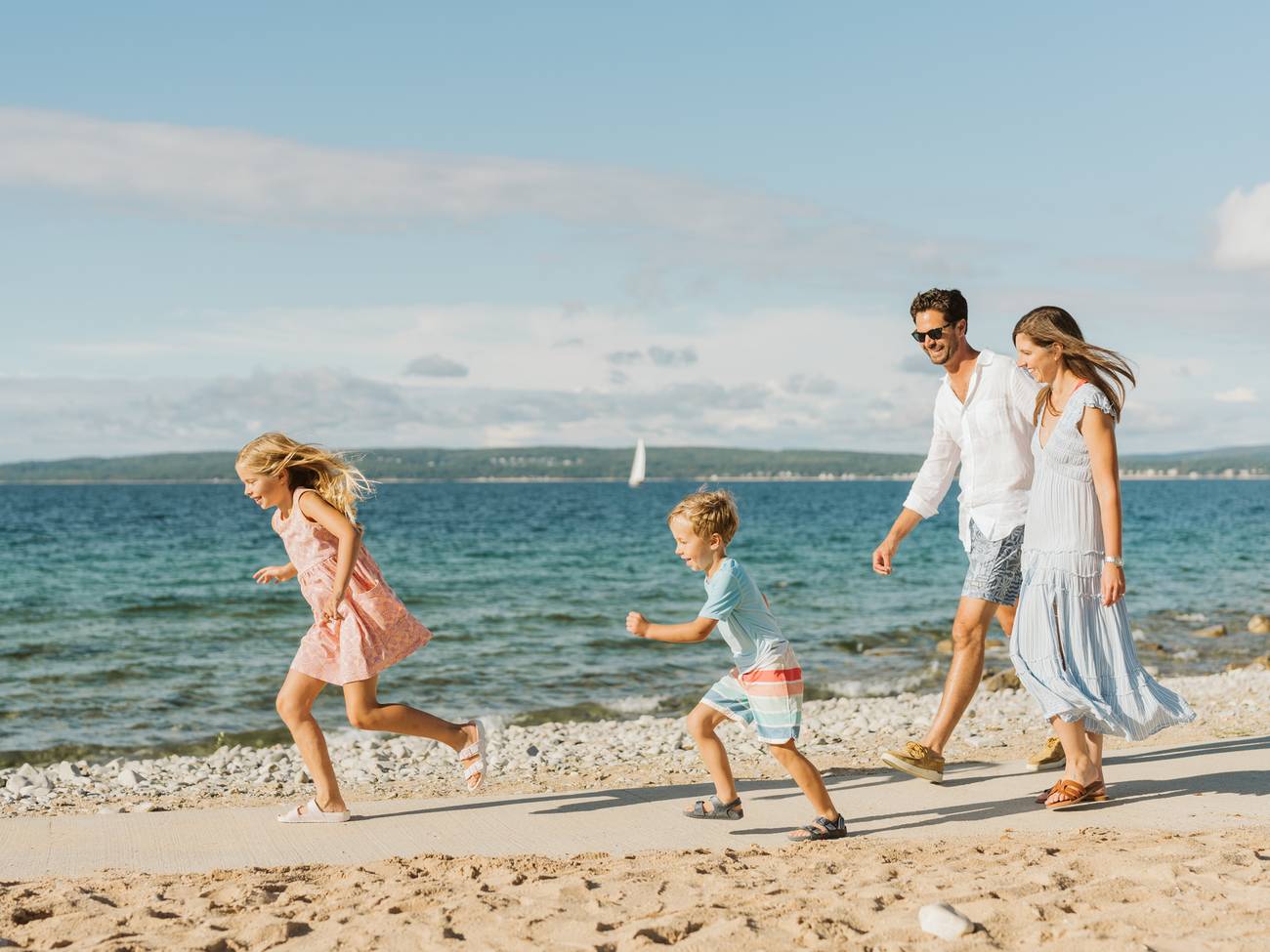 Smiling parents look on as kids run along waterfront sidewalk