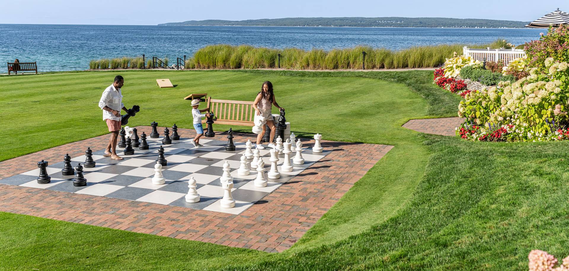 View of family playing giant chess on scenic lakefront game lawn alongside colorful flowers