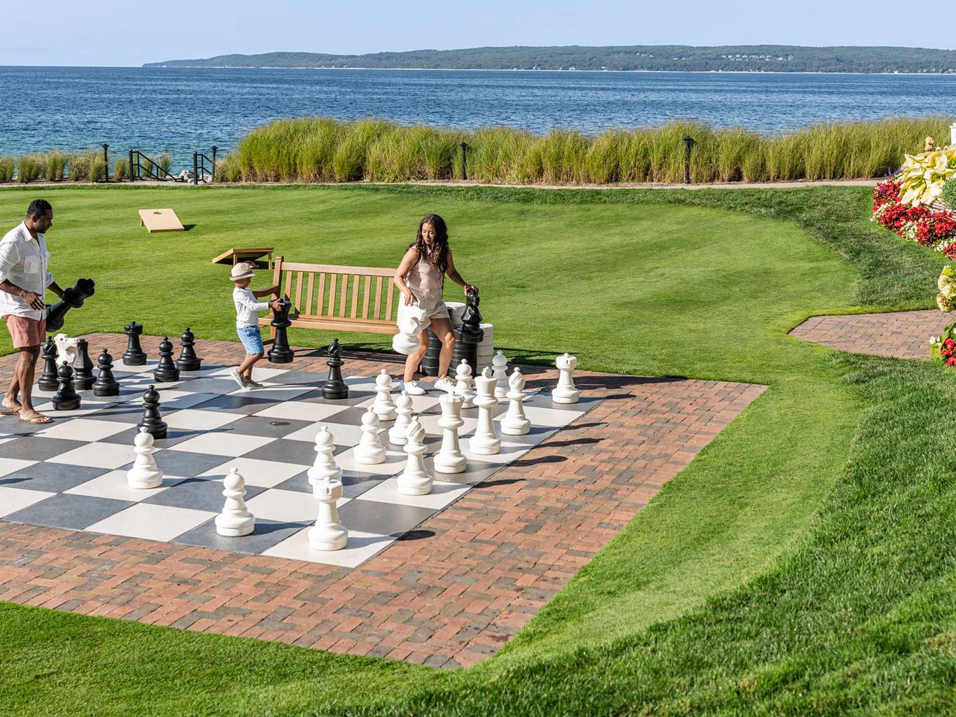 View of family playing giant chess on scenic lakefront game lawn alongside colorful flowers