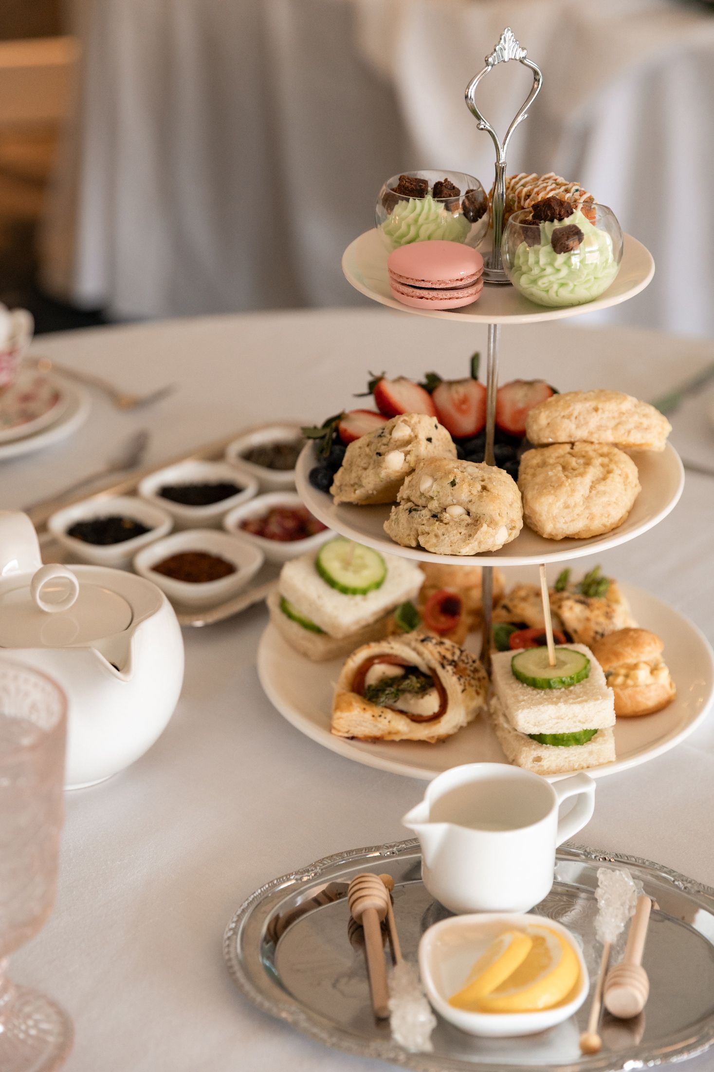 Tiered Afternoon Tea tray with sweets, scones, sandwiches, surrounded by teapot, cream, sugar