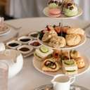 Tiered Afternoon Tea tray with sweets, scones, sandwiches, surrounded by teapot, cream, sugar