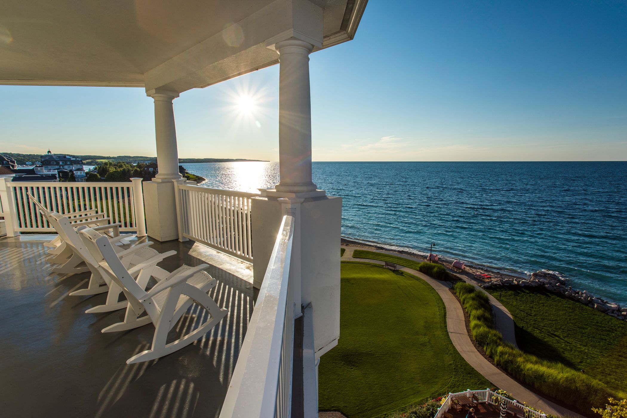 White rocking chairs on balcony that overlooks green lawns and Lake Michigan as the sun sets in the distance