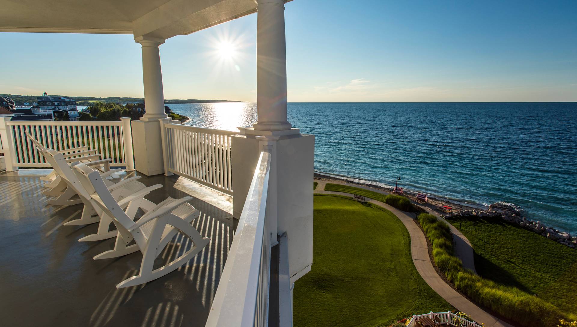 White rocking chairs on balcony that overlooks green lawns and Lake Michigan as the sun sets in the distance