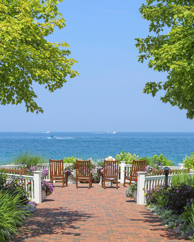 Boats drive by on Lake Michigan as guest looks on from garden rocking chairs