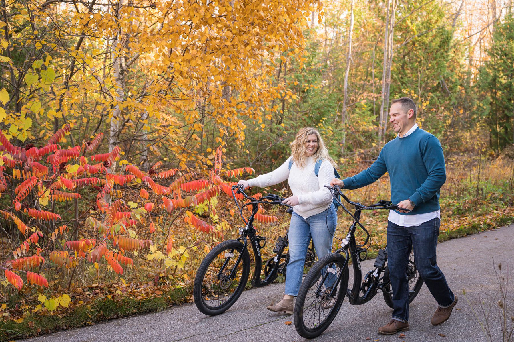 A couple walks their eBikes along a trail during the fall