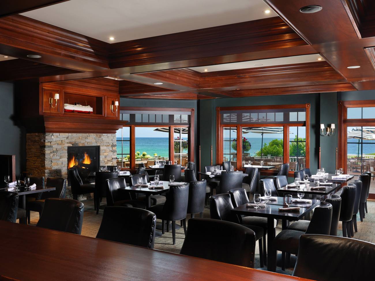 Vintage restaurant interior with fireplace and dark tables, chairs, overlooking patio and blue water view