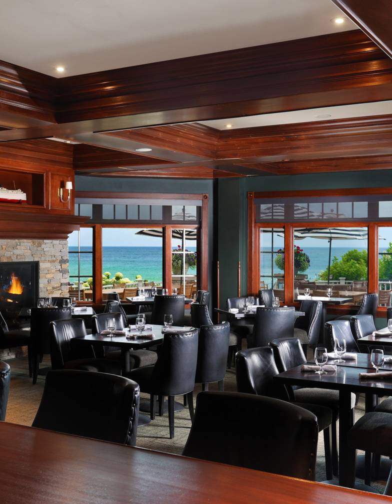 Vintage restaurant interior with fireplace and dark tables, chairs, overlooking patio and blue water view