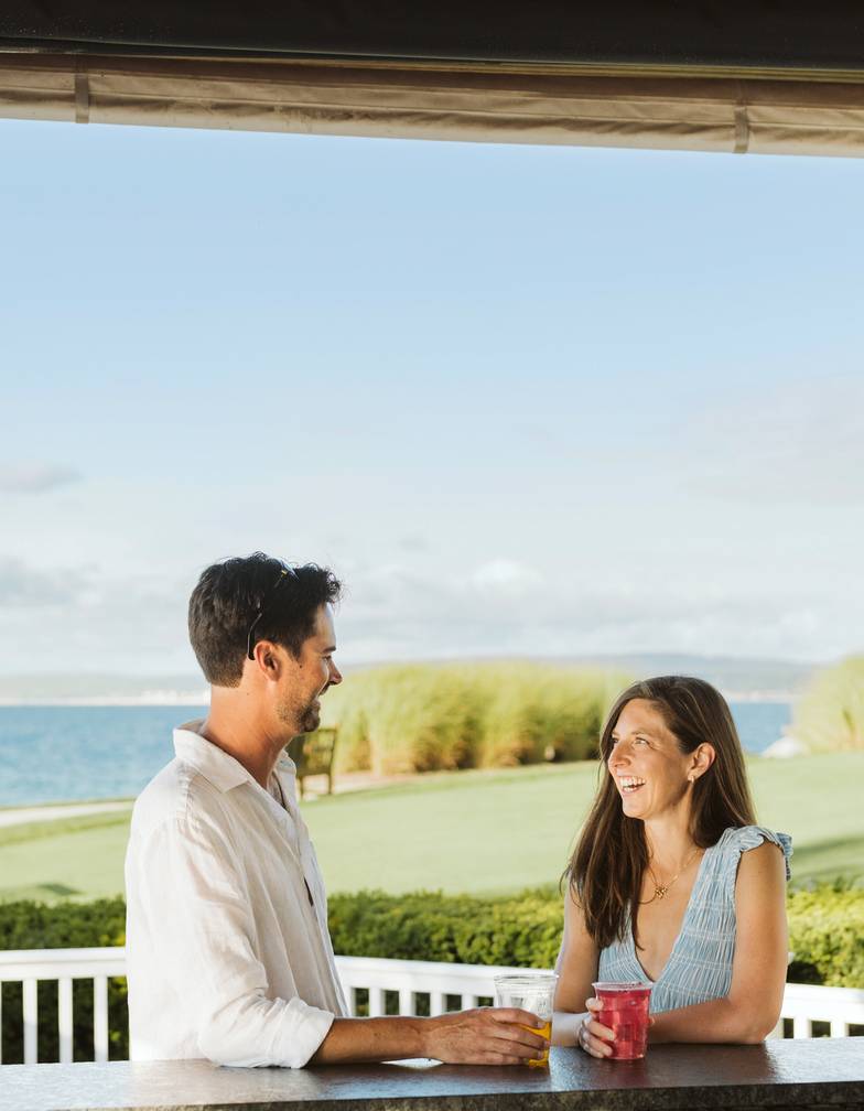 Laughing couple looks at each other over summer drinks at outdoor bar, Lake Michigan