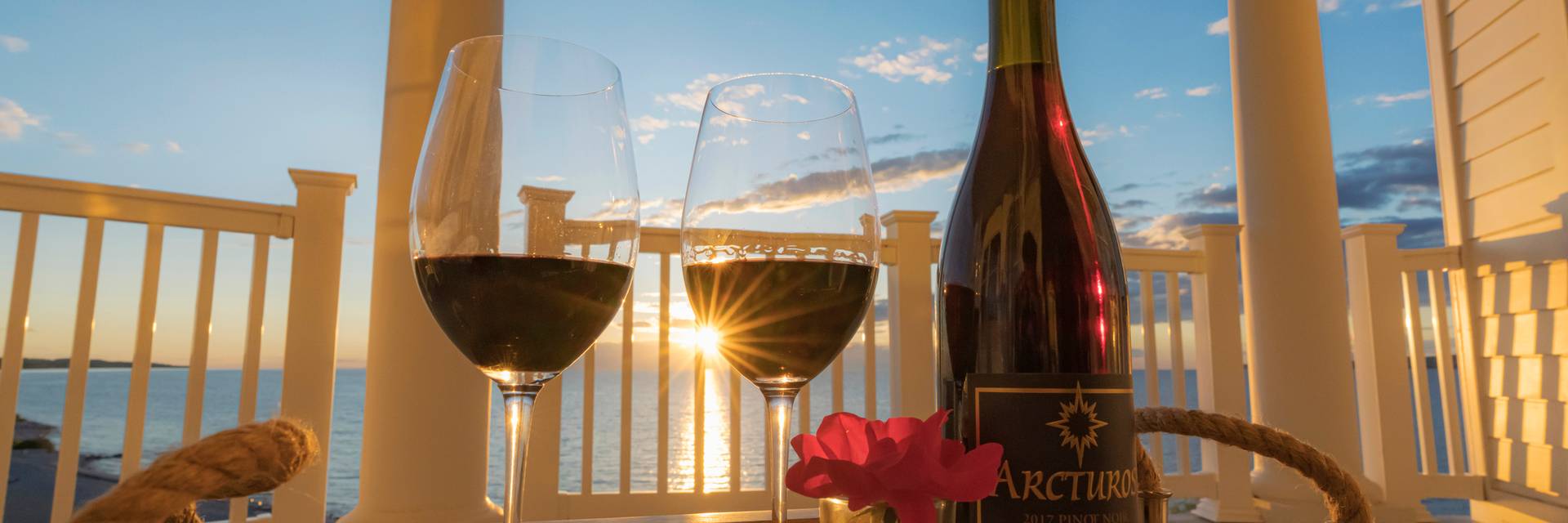 Tray of red wine glasses, bottle on balcony with yellow sunset rays over Lake Michigan