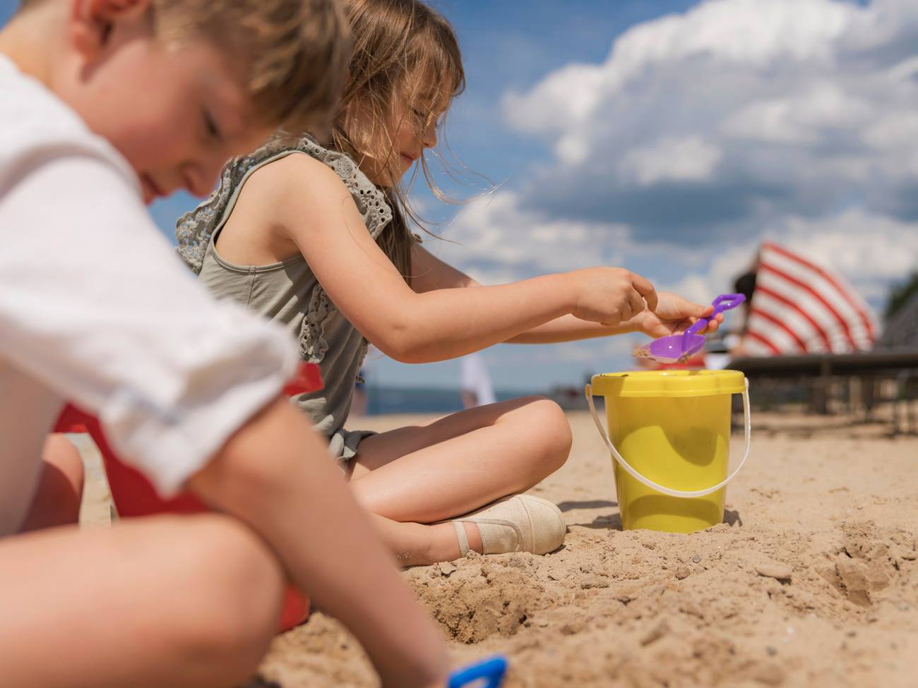 Siblings dig in beach sand under blue skies near beach loungers, Inn at Bay Harbor