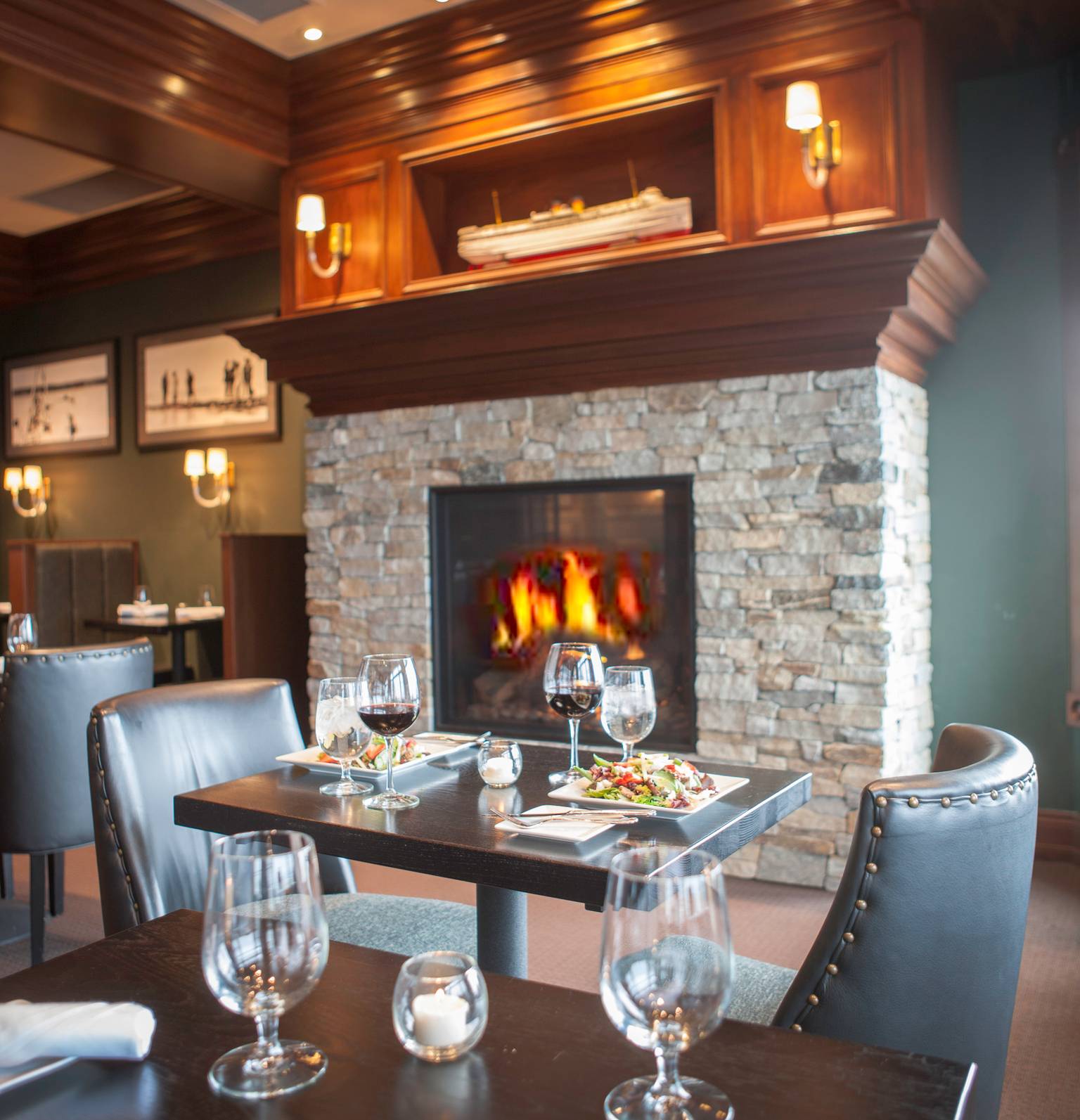 Table for two in front of stone and wood fireplace, set with wine, water goblets, and salads, Vintage Chophouse | Wine Bar