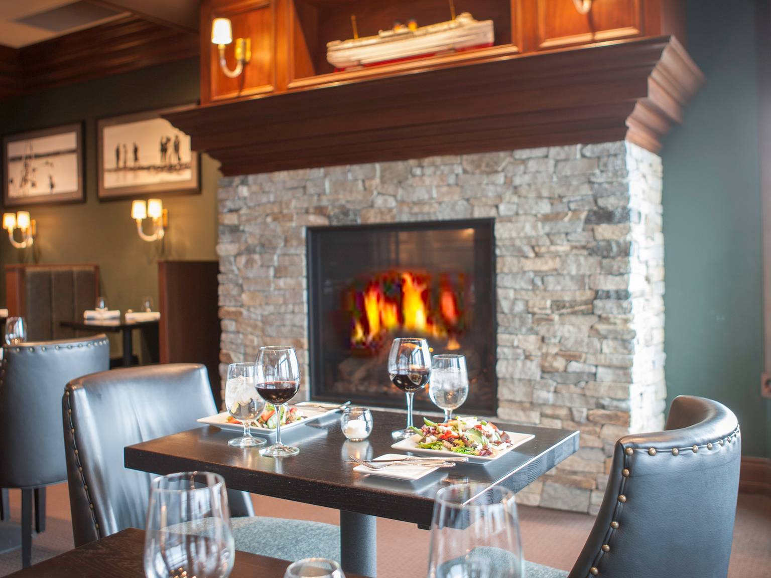 Table for two in front of stone and wood fireplace, set with wine, water goblets, and salads, Vintage Chophouse | Wine Bar
