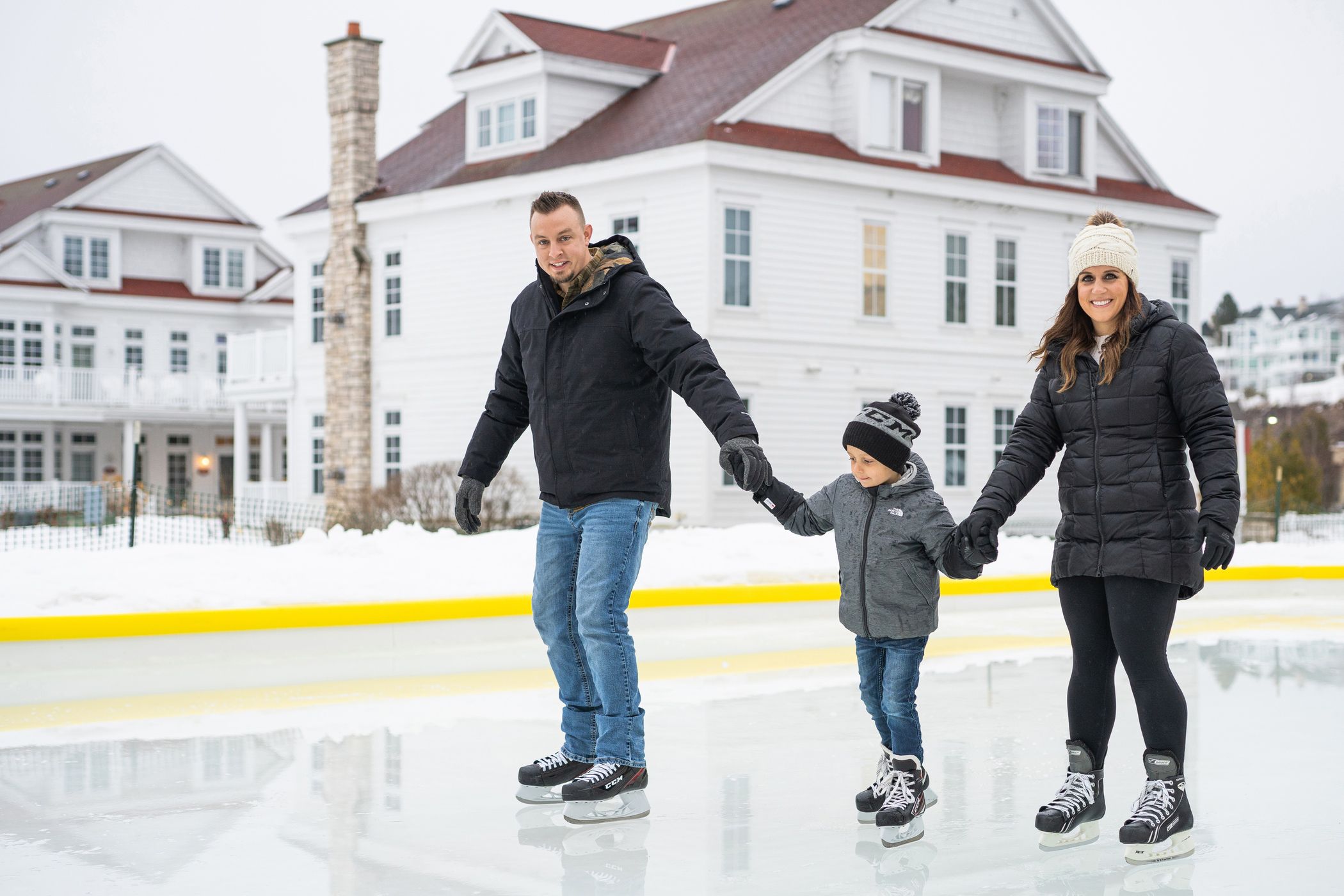 Young mom and dad hold hands with child at outdoor ice rink, Cottages at Bay Harbor