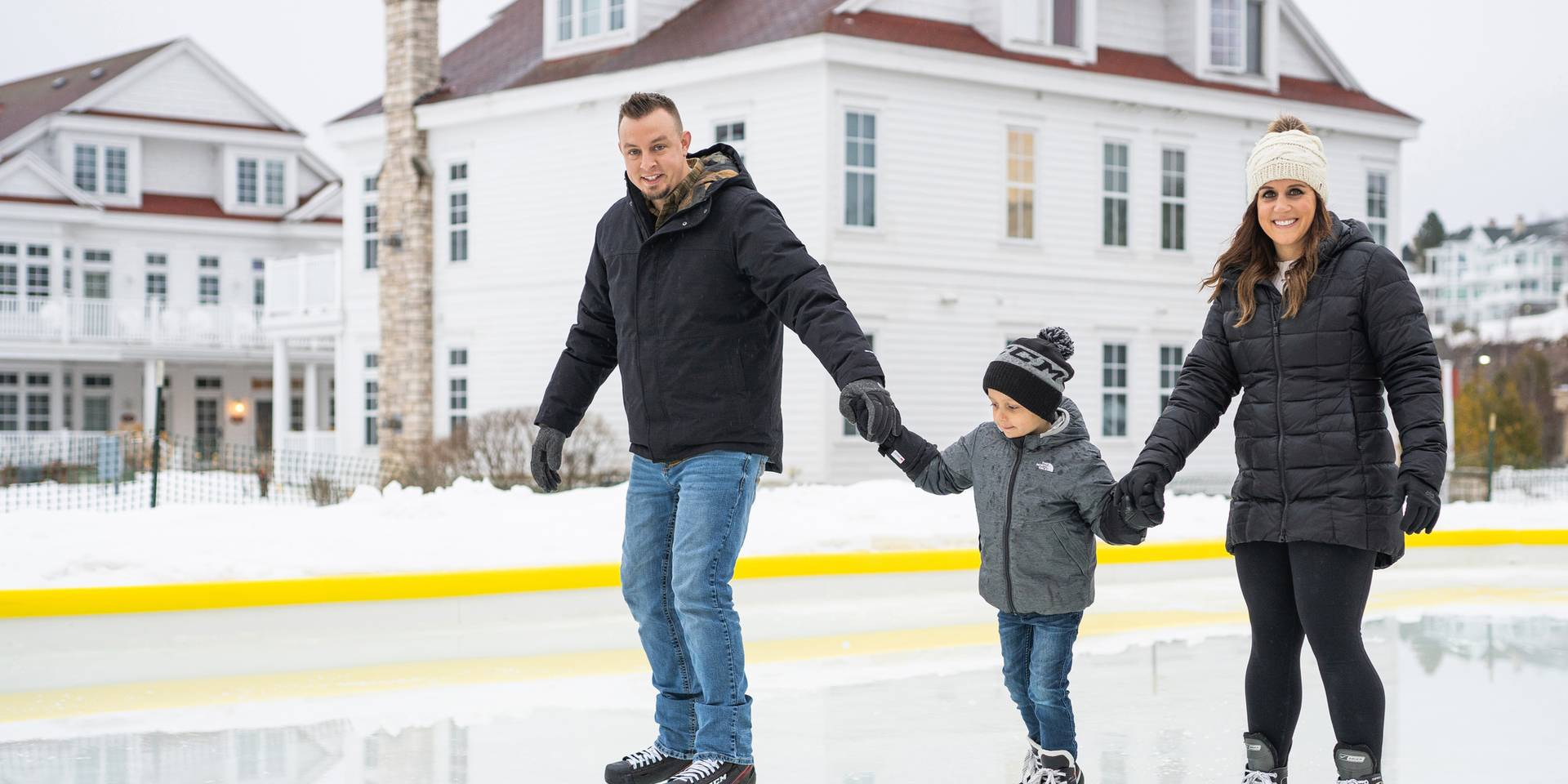 Young mom and dad hold hands with child at outdoor ice rink, Cottages at Bay Harbor