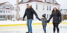 Young mom and dad hold hands with child at outdoor ice rink, Cottages at Bay Harbor