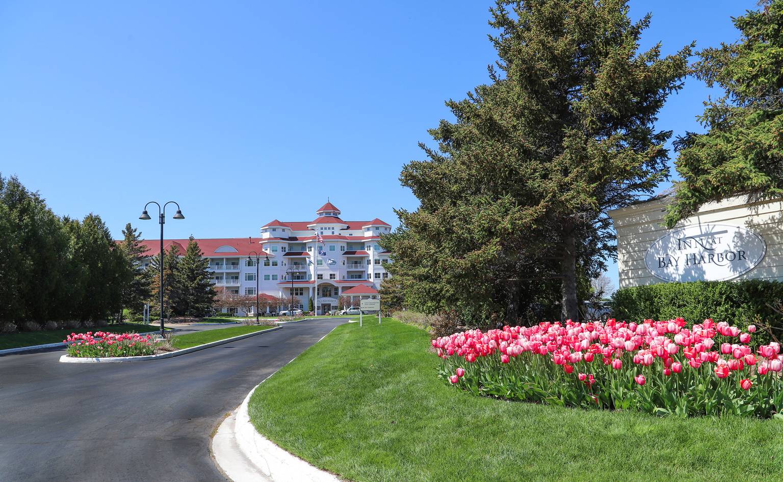 Bright pink tulips blooming near front entry sign and drive of Inn at Bay Harbor under blue skies
