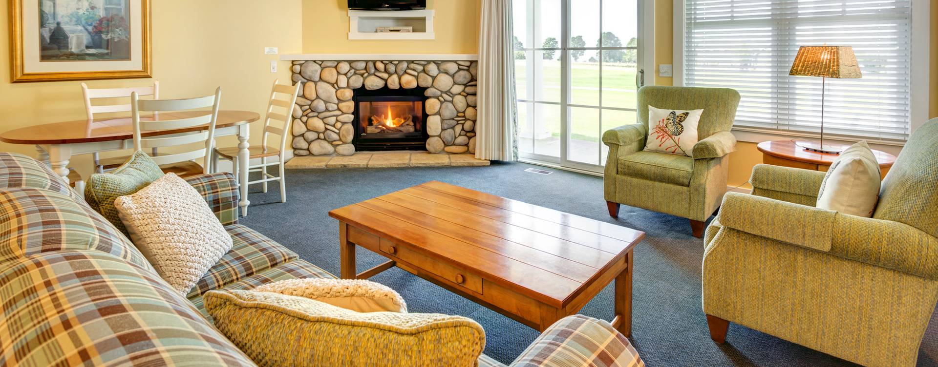 Wide view of living area with stone fireplace, couch and chairs, Crooked Tree Cottages