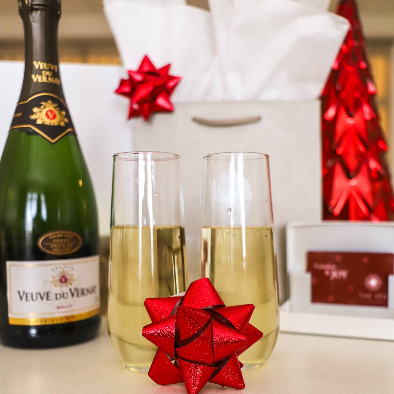 Red bow on champagne glasses near wine bottle, holiday shopping bags