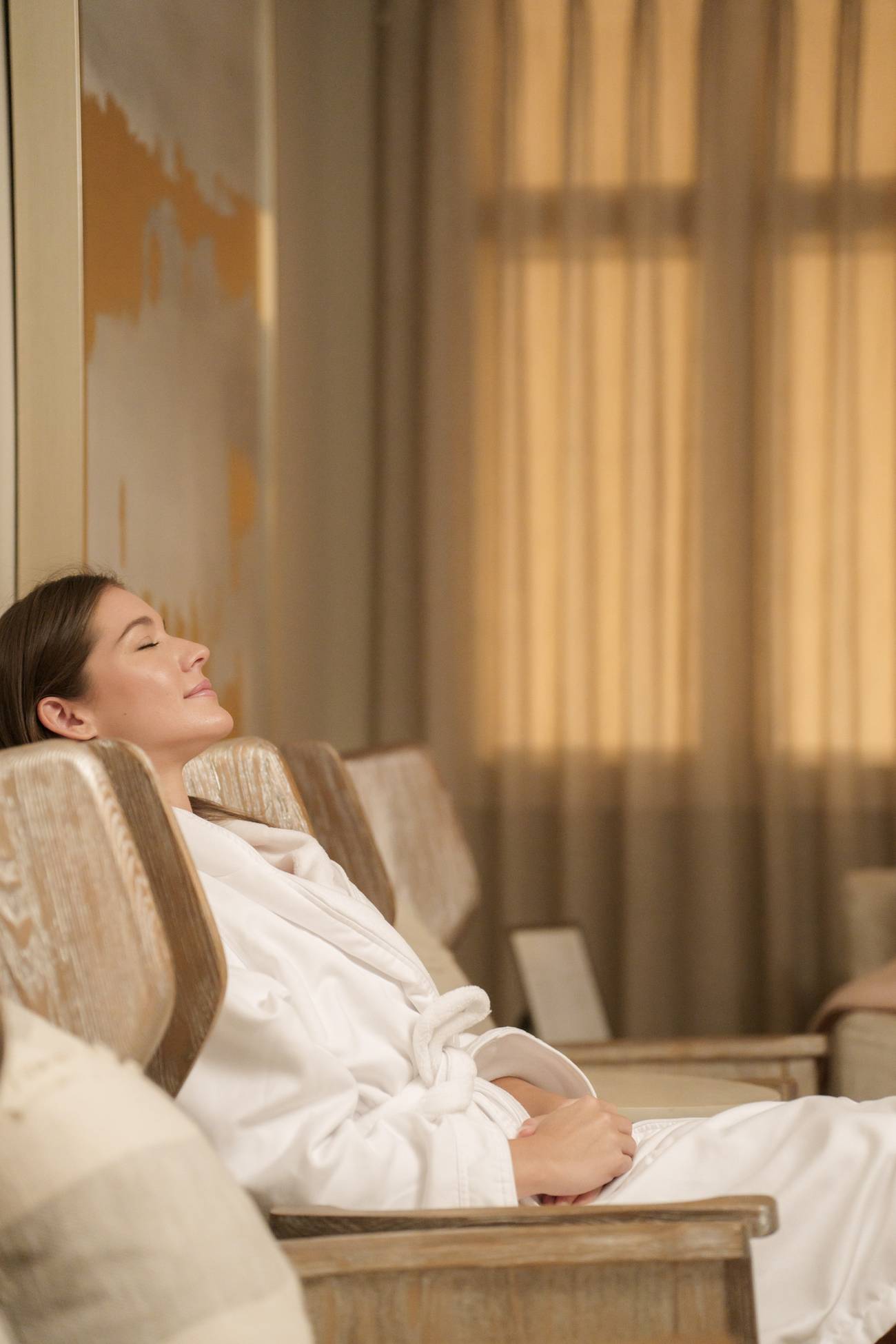 Side view of young woman relaxing with closed eyes in wooden chair at The Spa's relaxation lounge