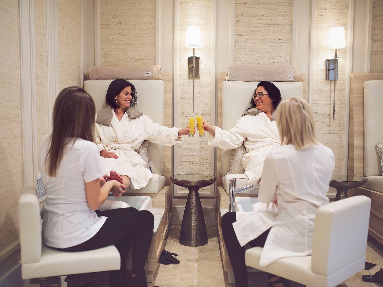 Two woman cheers mimosas while getting pedicures