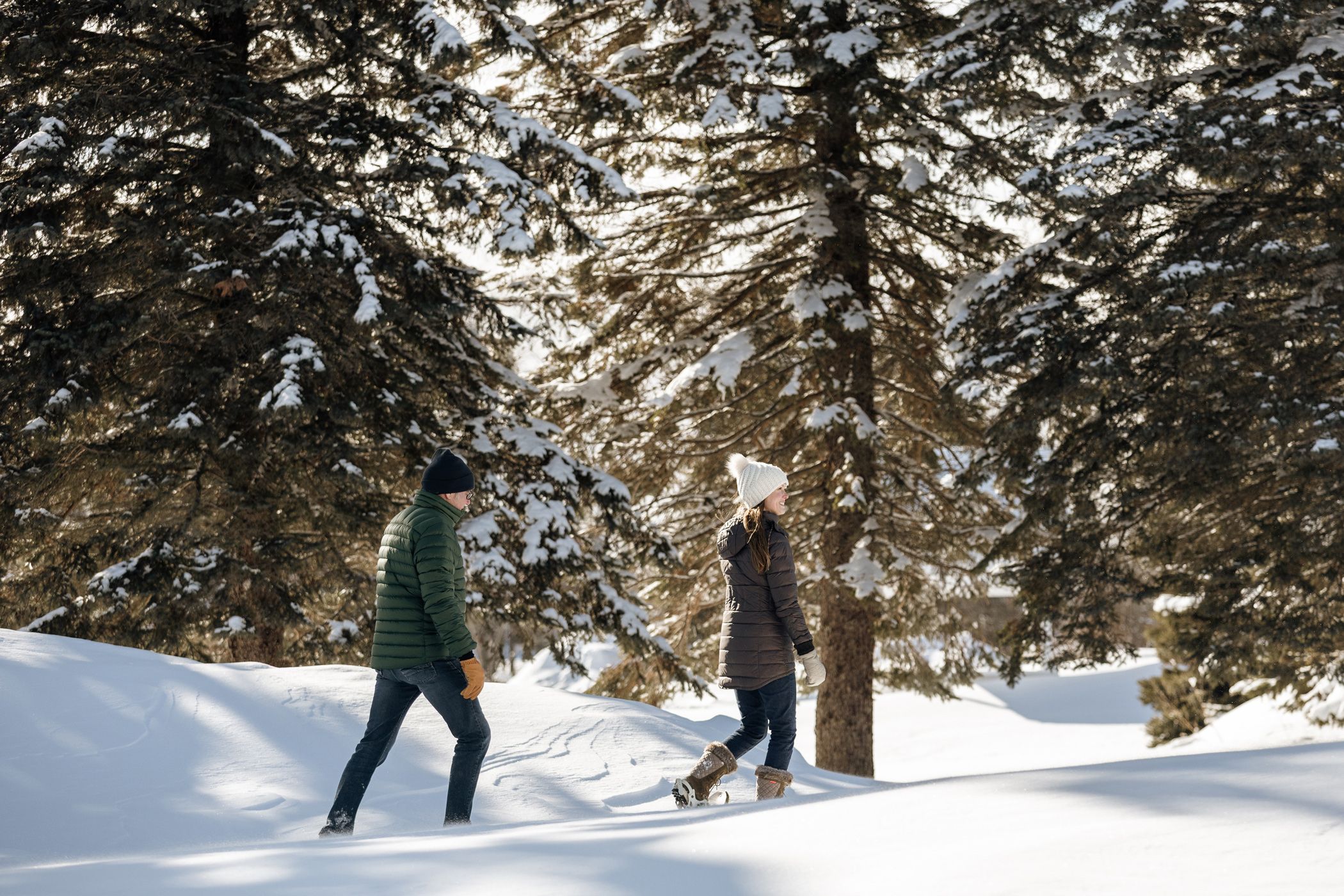 Winter-clad couple walks through snowy pine forest