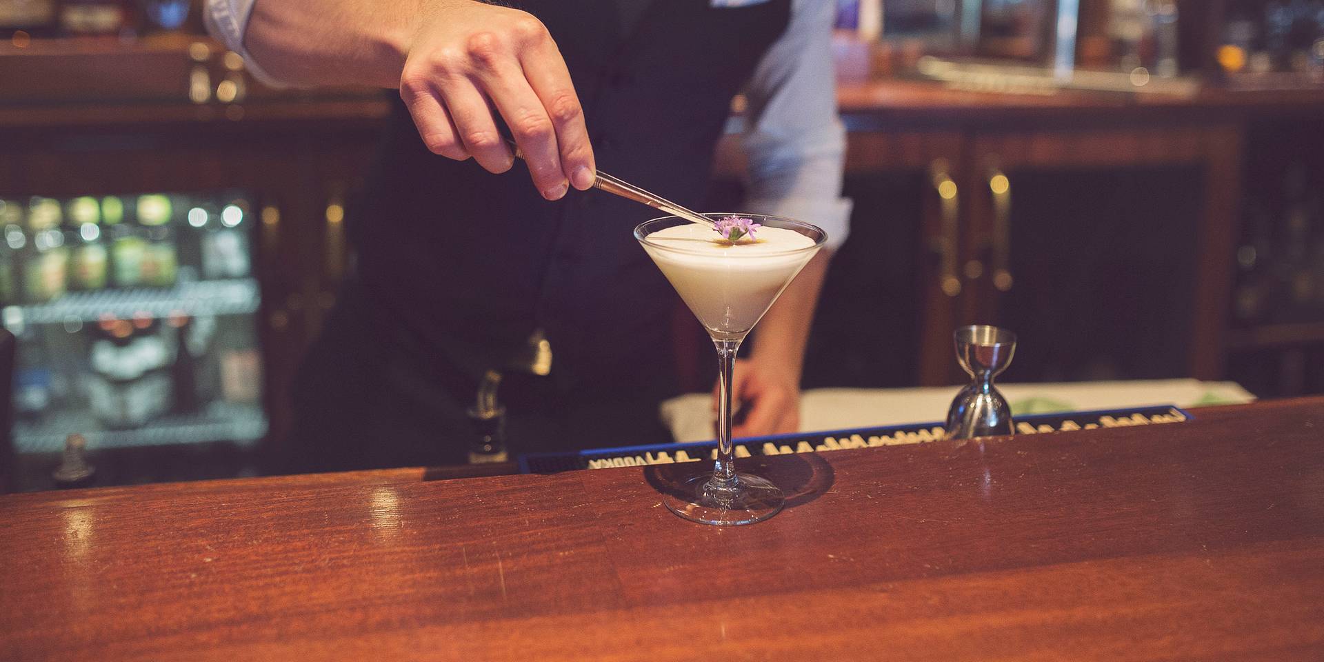 A bartender places a flower on a craft cocktail
