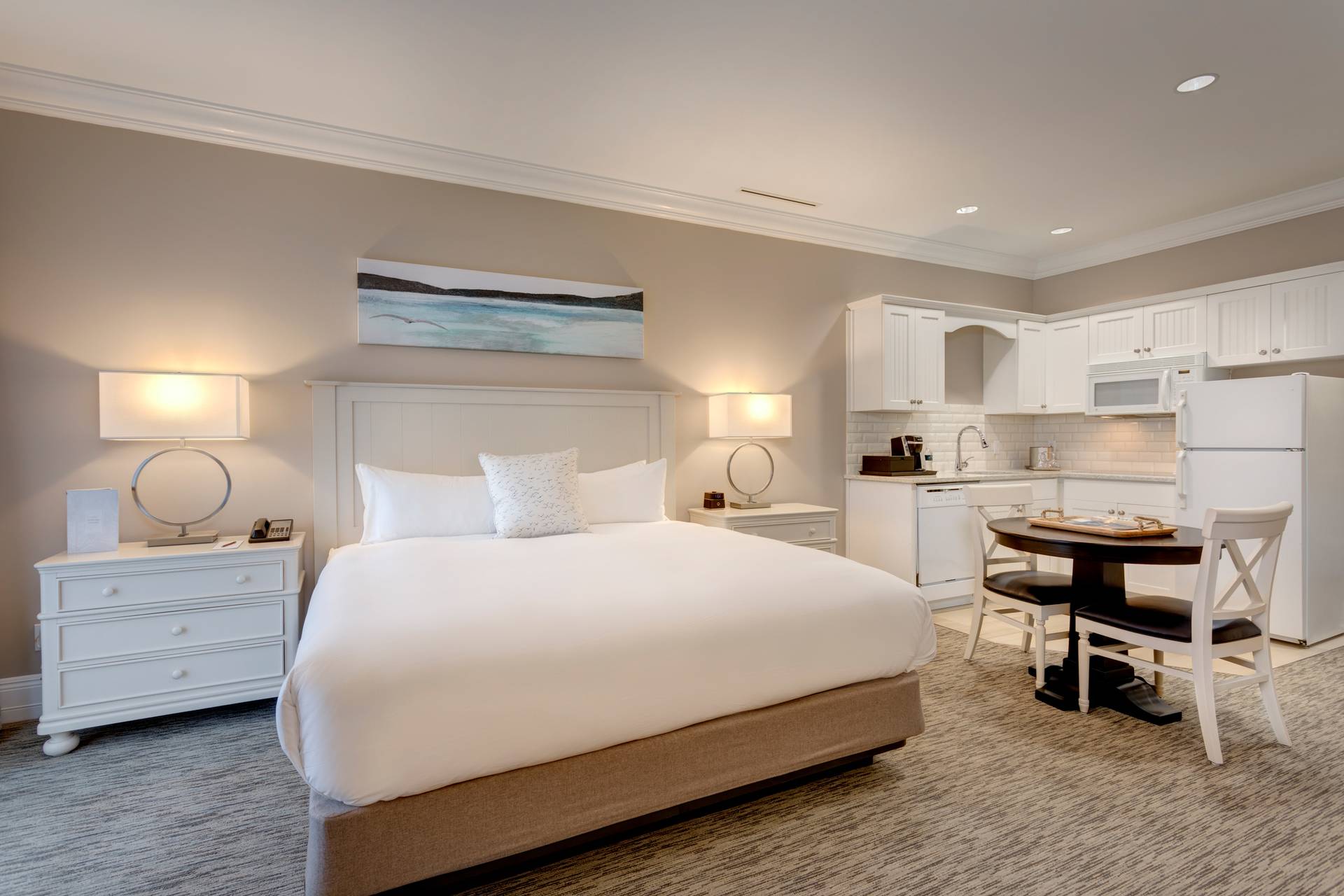 Hotel room with white king bed, corner kitchenette, and dining chair, Inn at Bay Harbor