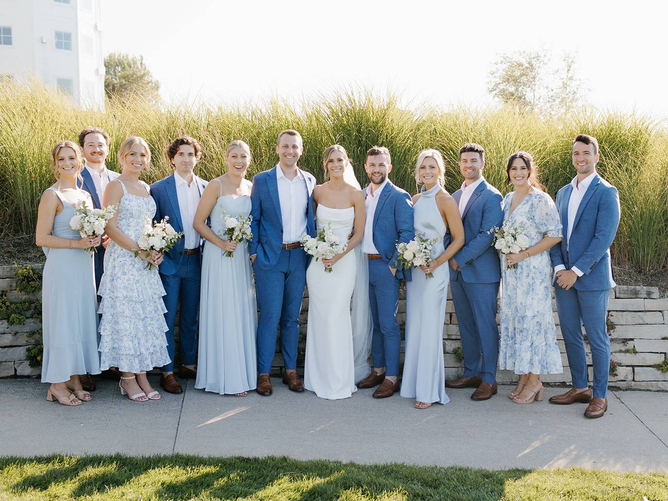 Wedding party wearing shades of blue poses in front of dune grass