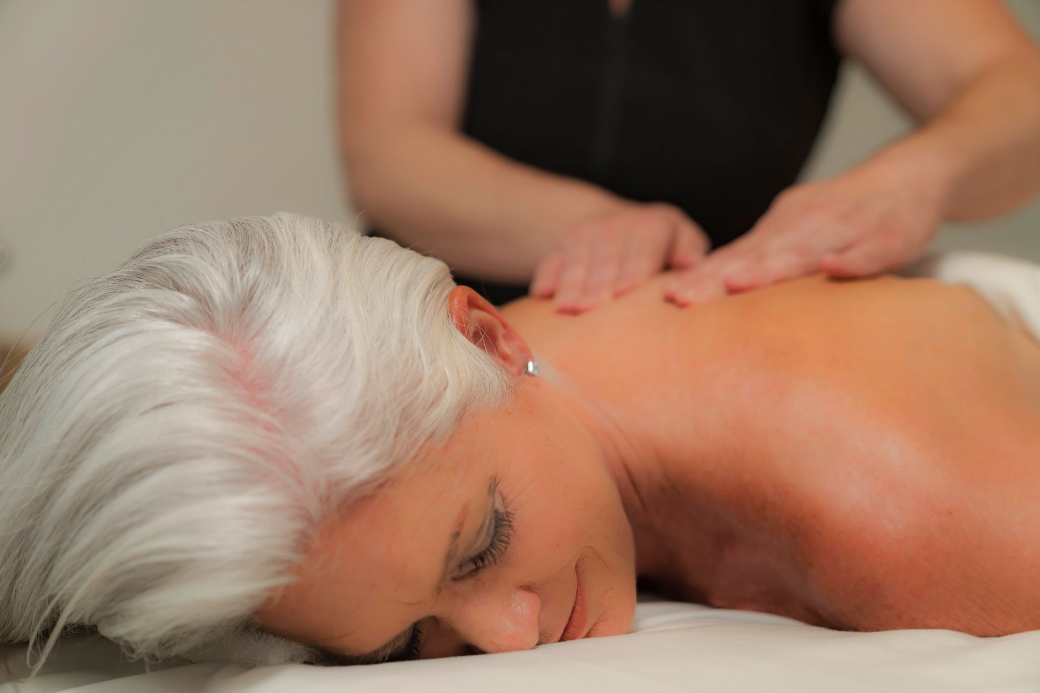 Gray haired woman smiles slightly as she receives relaxing massage