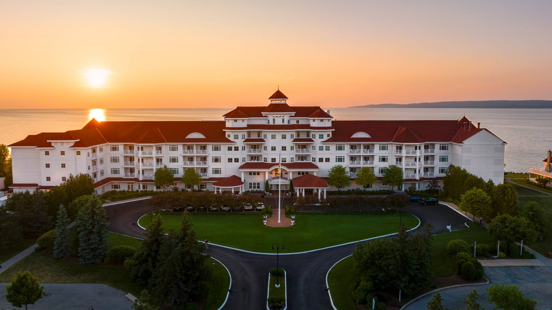 Aerial view of Inn at Bay Harbor front exterior as orange sunset forms over Lake Michigan