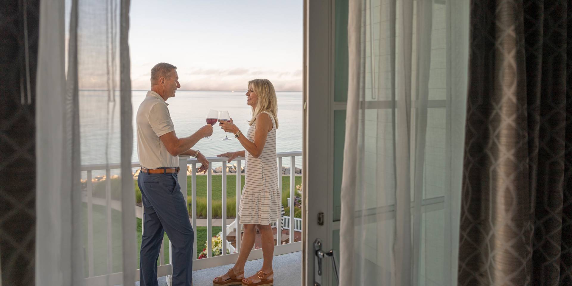 Smiling senior couple toasts with red wine on lake view balcony, Inn at Bay Harbor