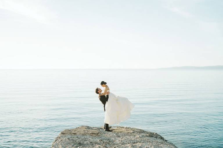 Groom lifts bride in the air in front of calm blue Lake Michigan