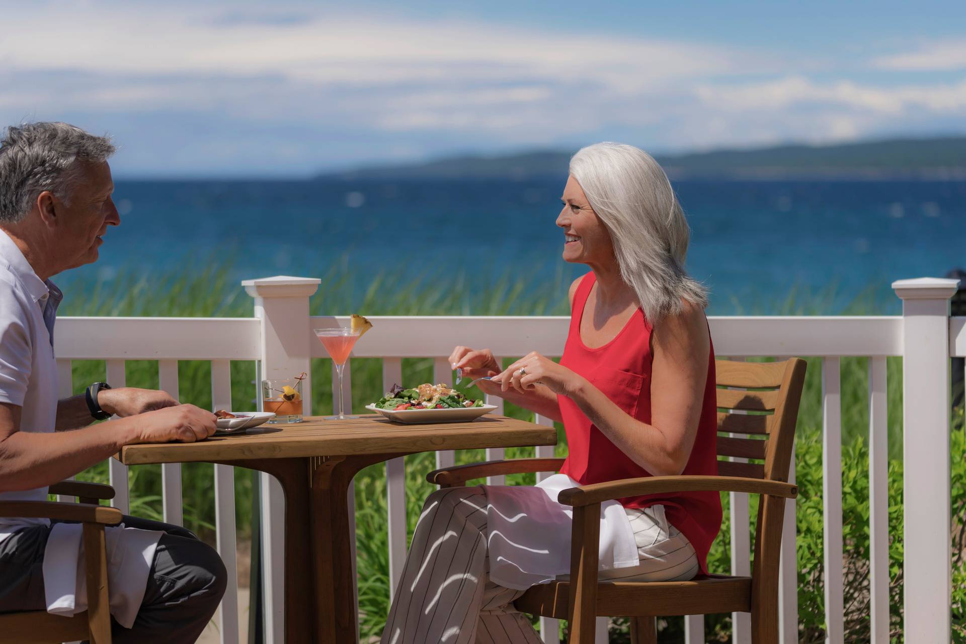 Senior couple eats lunch with cocktails on waterfront outdoor patio, Vintage at Inn at Bay Harbor
