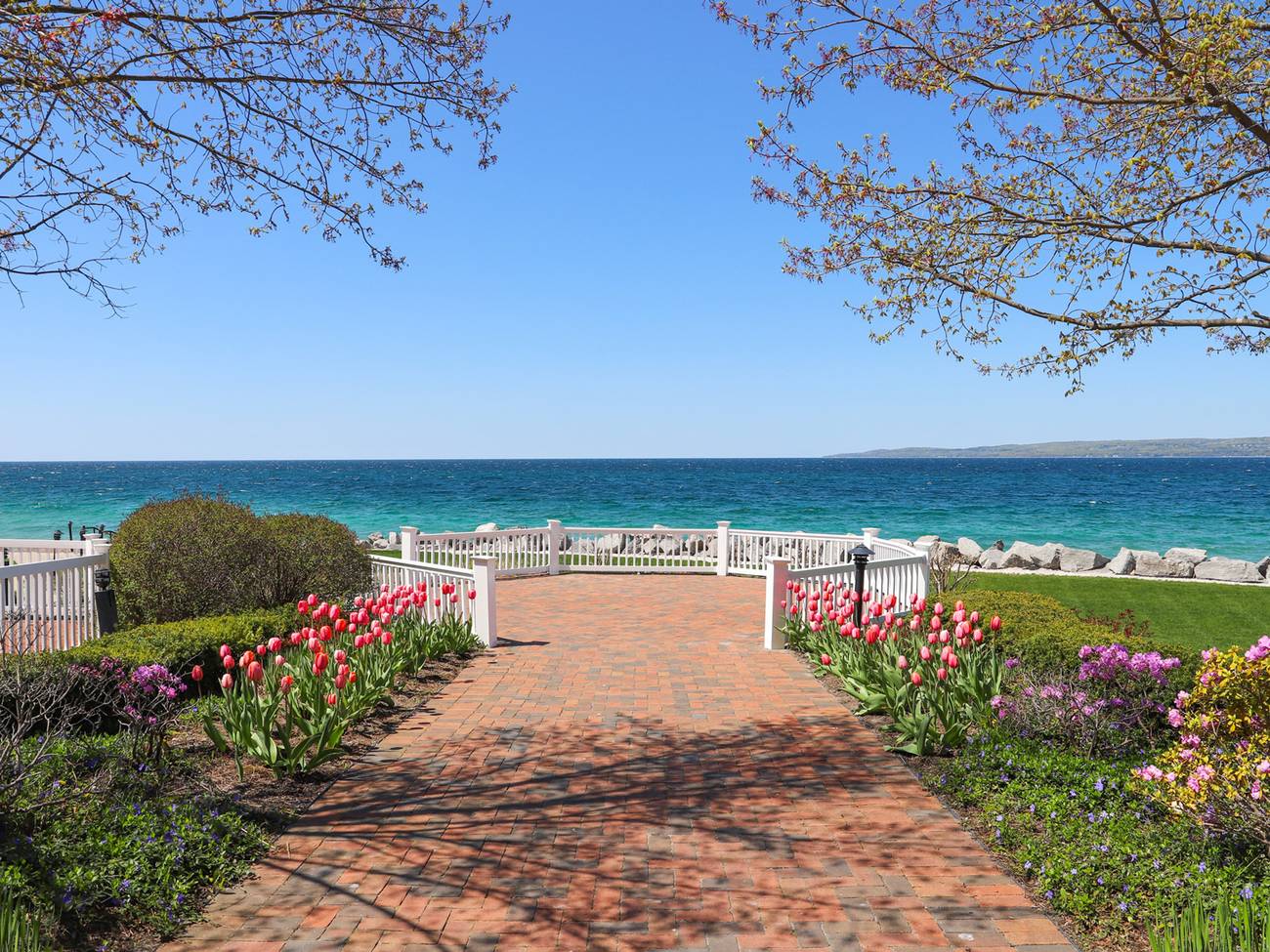 Tulips and budding trees surrounding Inn at Bay Harbor brick patio overlooking bright blue water of Lake Michigan